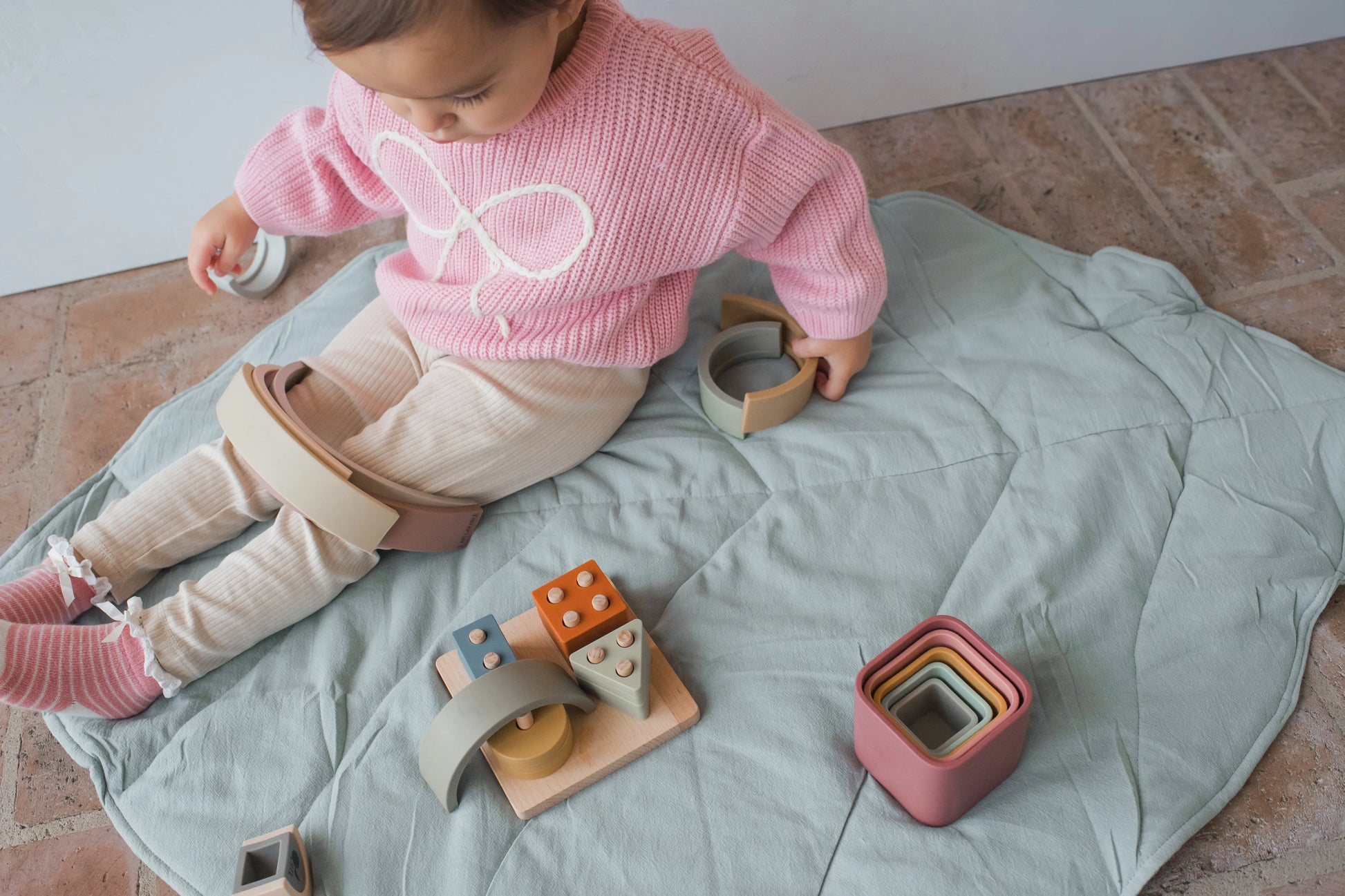 Toddler playing with rainbow stacker on cotton play mat