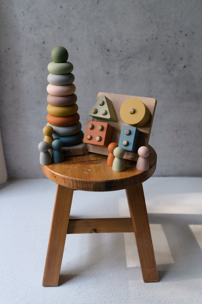 Sensory Starter Kit with Mini Silicone Peg Dolls, Shape Puzzle, and Ring Stacker displayed on a wooden stool