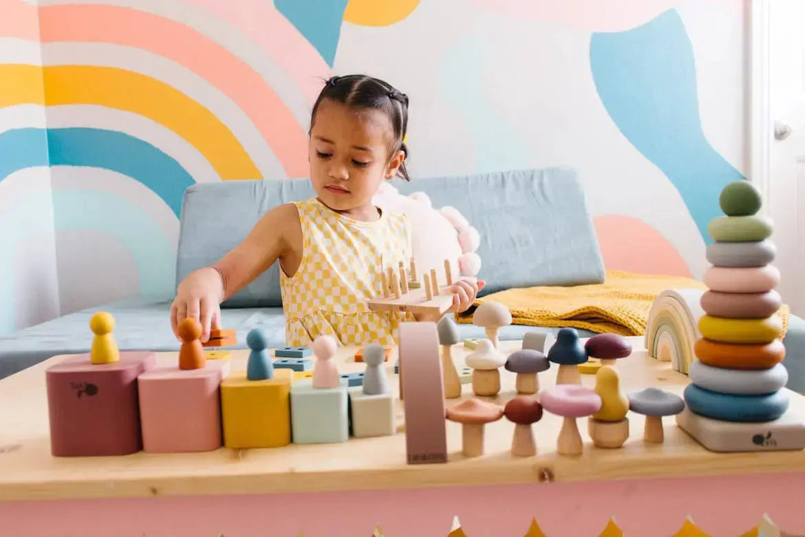 Toddler playing with Montessori toy bundle including stacking cups, rainbow, puzzle, and mini Silicone peg dolls