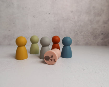 Set of colorful silicone pegs or mini dolls on a light surface with a gray background that shows LYTL logo