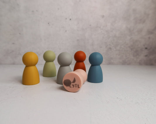 Set of colorful silicone pegs or mini dolls on a light surface with a gray background that shows LYTL logo